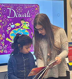 Teacher aids student in reading a book about Diwali